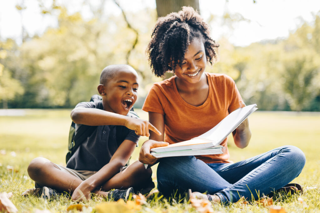 Two children reading together on the grass as part of a summer learning activity