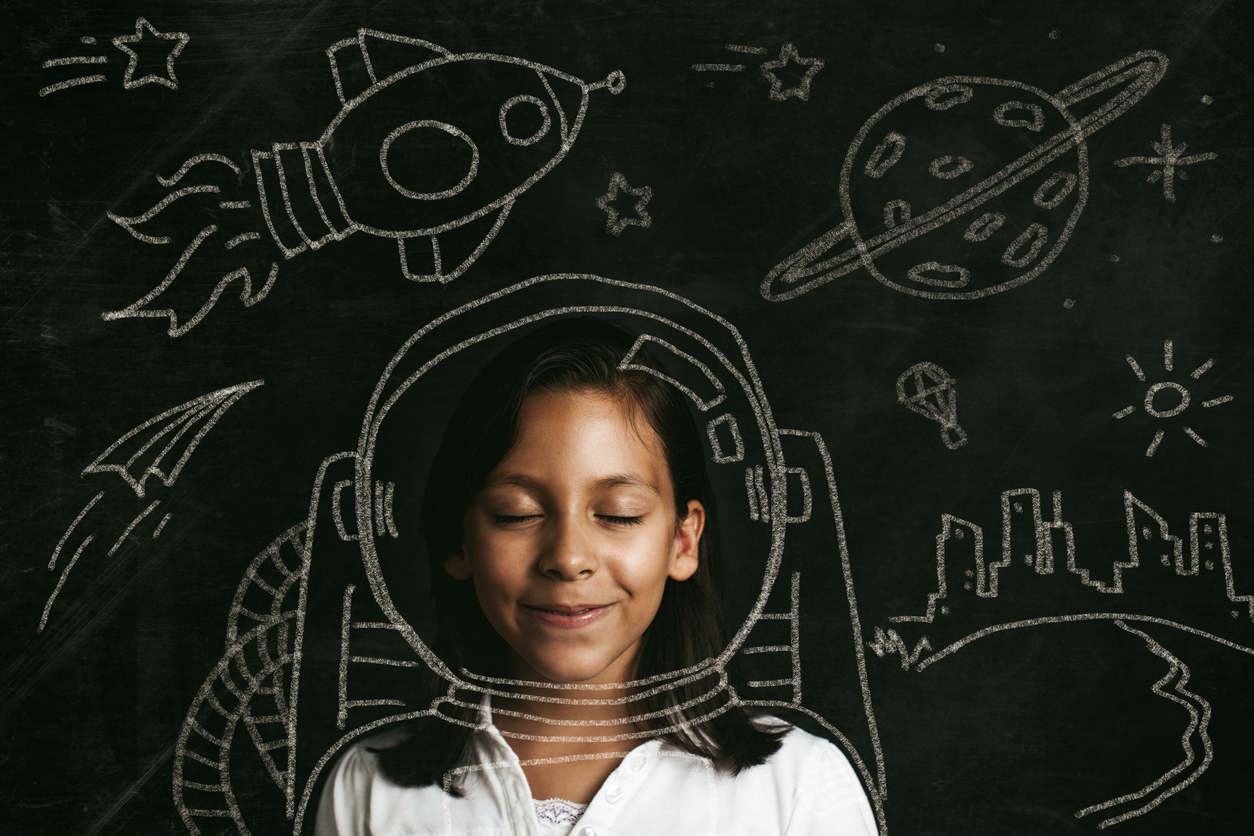 young girl standing in front of a blackboard with chalk drawings of outer space.