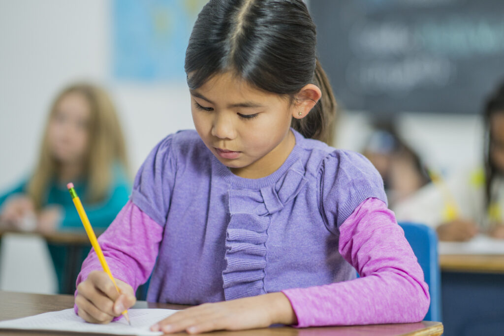 little girl with a purple shirt, sitting at a desk taking a test