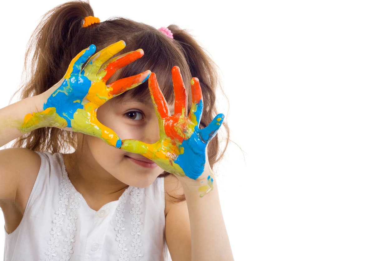 A young girl holds up her painted hands while smiling and depicts one of The Learning Lab’s core values: an attitude of gratitude