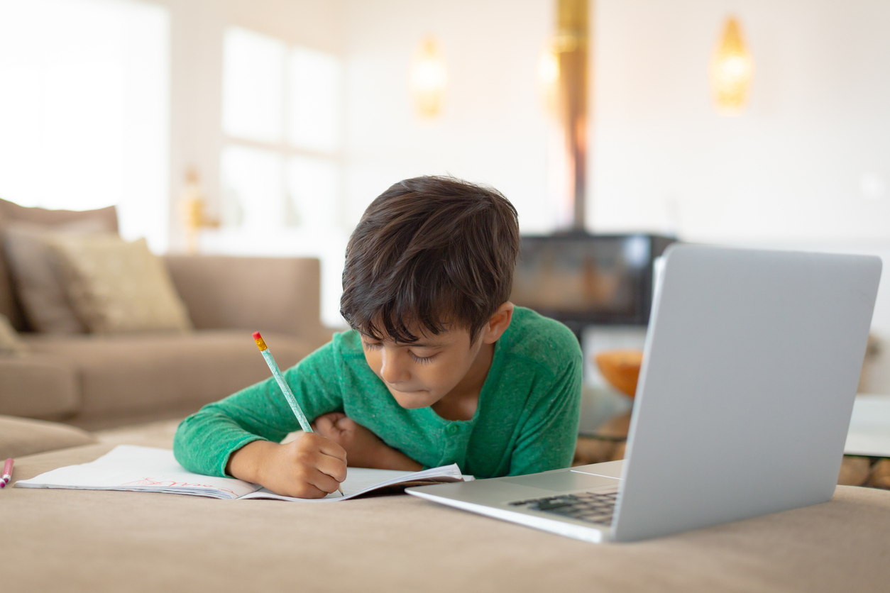 boy using laptop while drawing a sketch on book at home